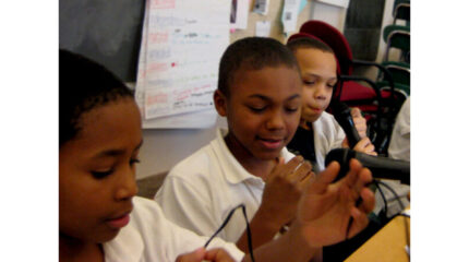 Three youth speaking into microphones in a classroom