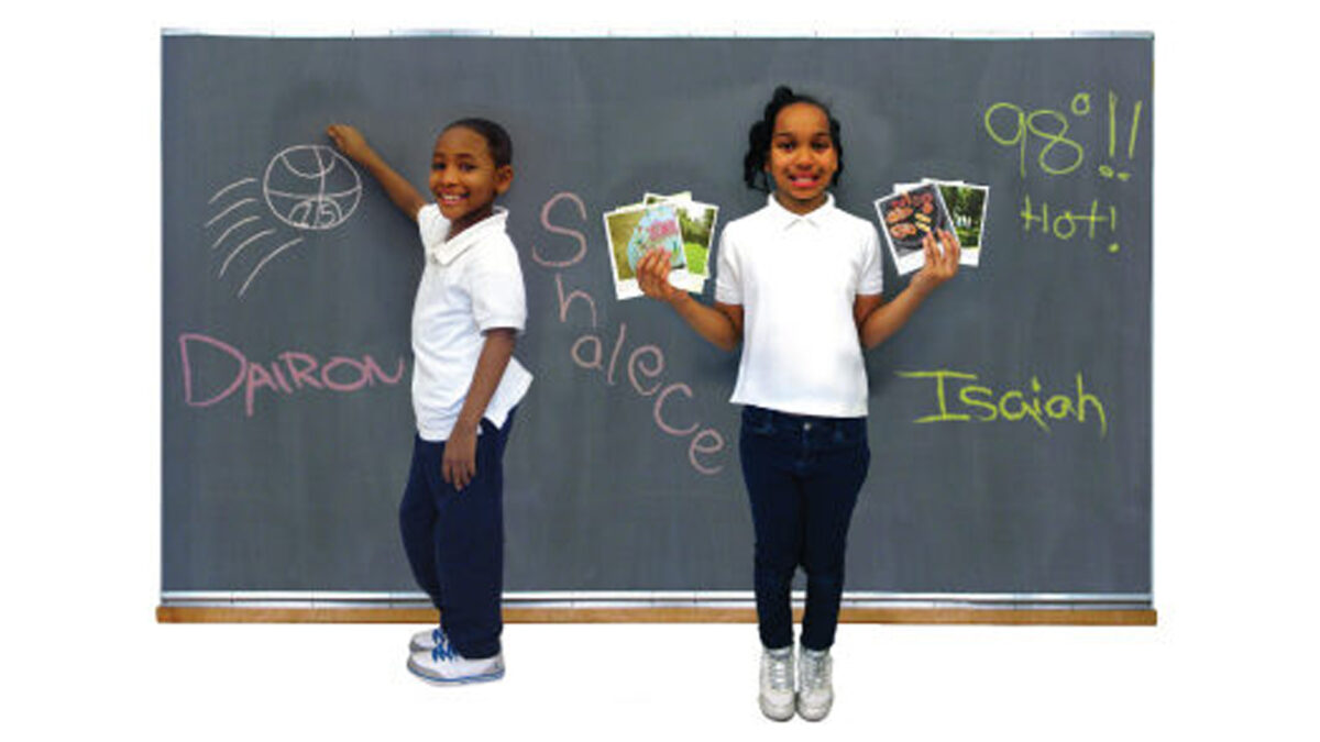 Two youth smiling and standing in front of a chalkboard