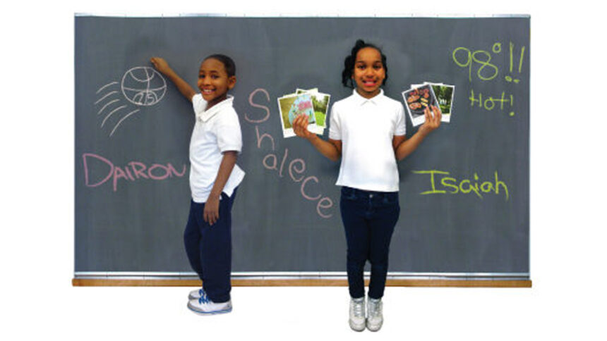 Two youth smiling and standing in front of a chalkboard