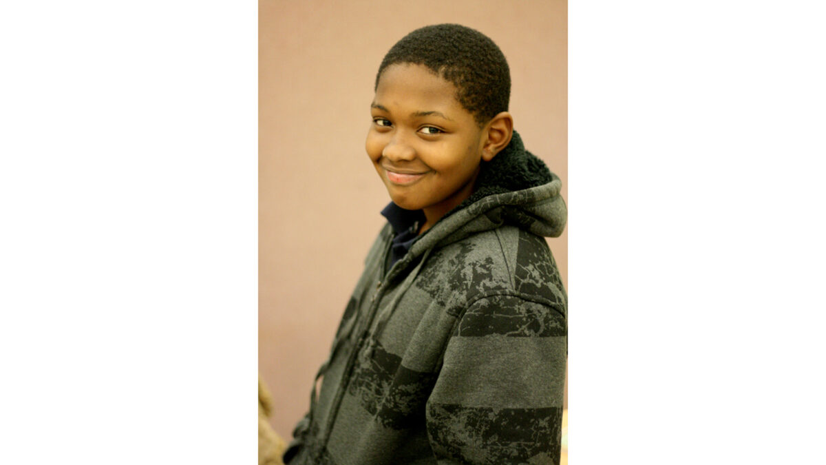 A youth wearing a hoodie smiling at the camera