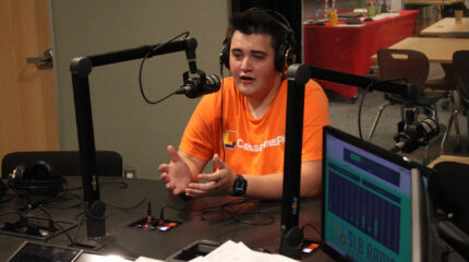 A teen wearing headphones speaking into a microphone in a radio studio