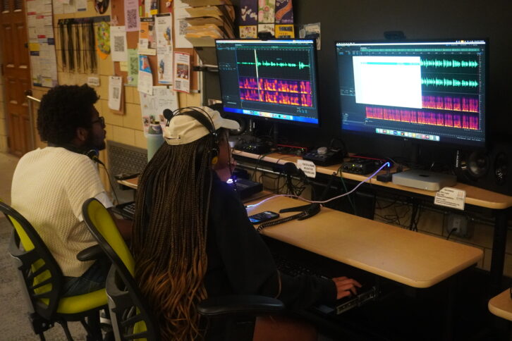 Two teens wearing headphones looking at audio editing software on computers