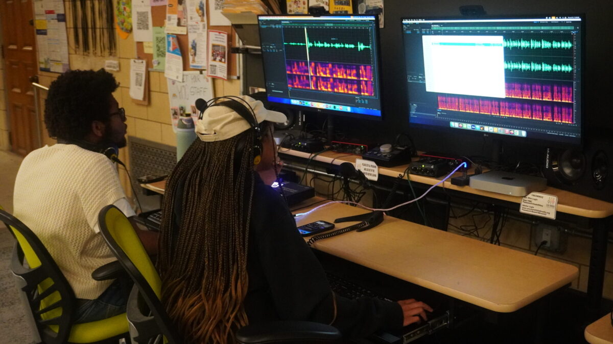 Two teens wearing headphones looking at audio editing software on computers