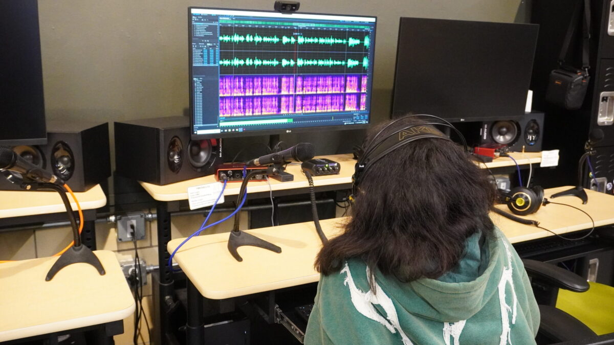 A teen wearing headphones looking at audio editing software on a computer