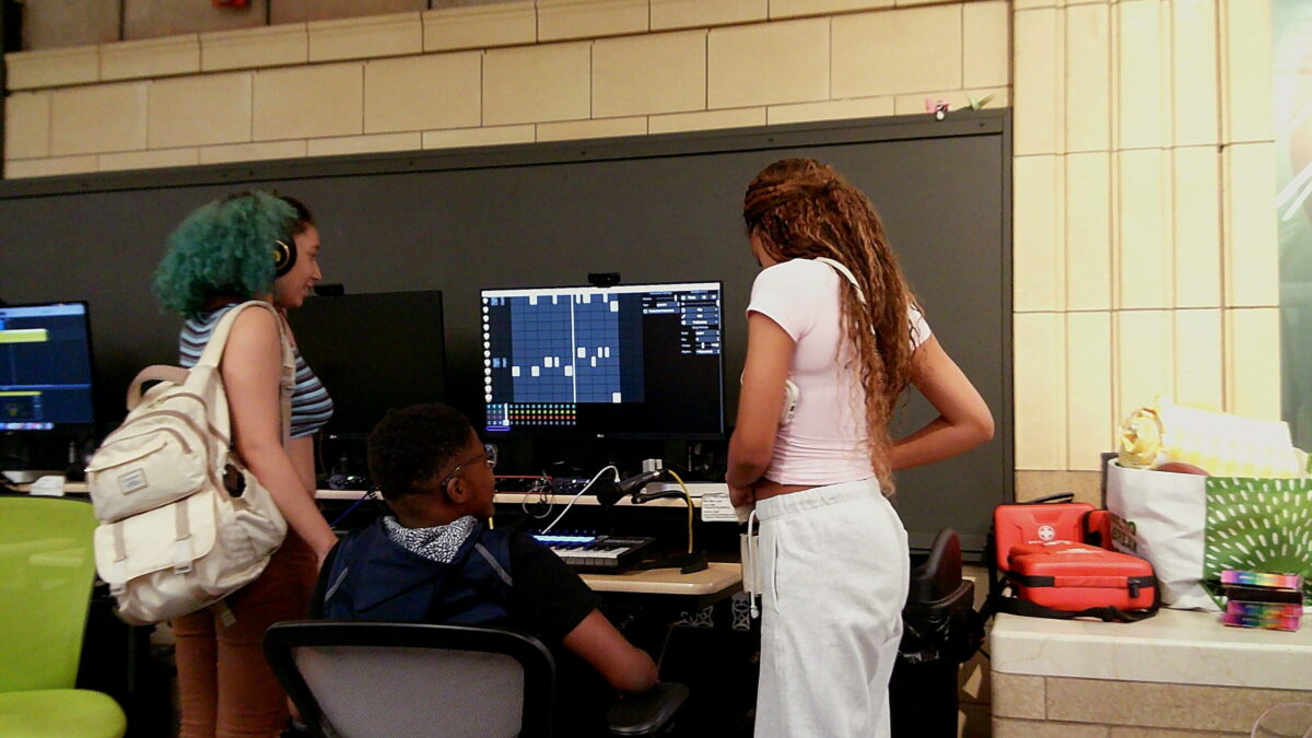 Rhyme and Reason-3 two teens stand near a computer while a third works at the monitor.