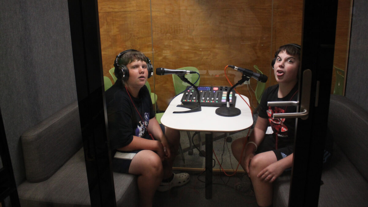 FYV-2 Two youth wearing headphones sitting behind microphones and making funny faces in a recording booth