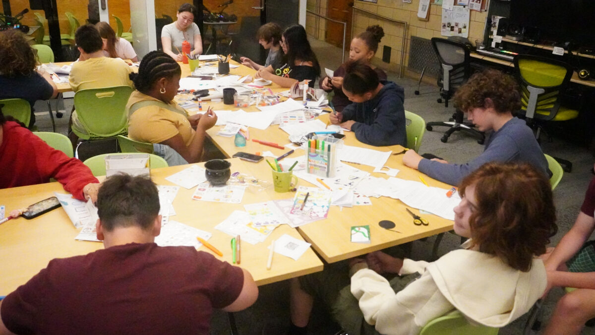 FYV-7 Twelve youth and an adult drawing on pieces of paper sitting at tables