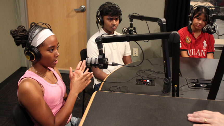 Three teens wearing headphones speaking into microphones in a radio studio
