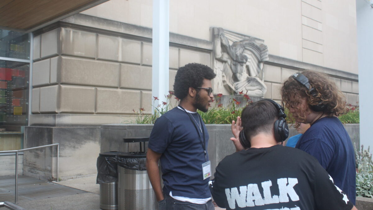 Three teens, two wearing headphones, standing in front of a marble building