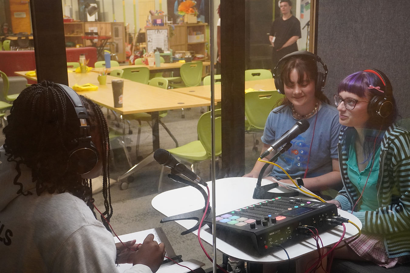 Three teens wearing headphones sitting around microphones and an audio mixer in a recording pod