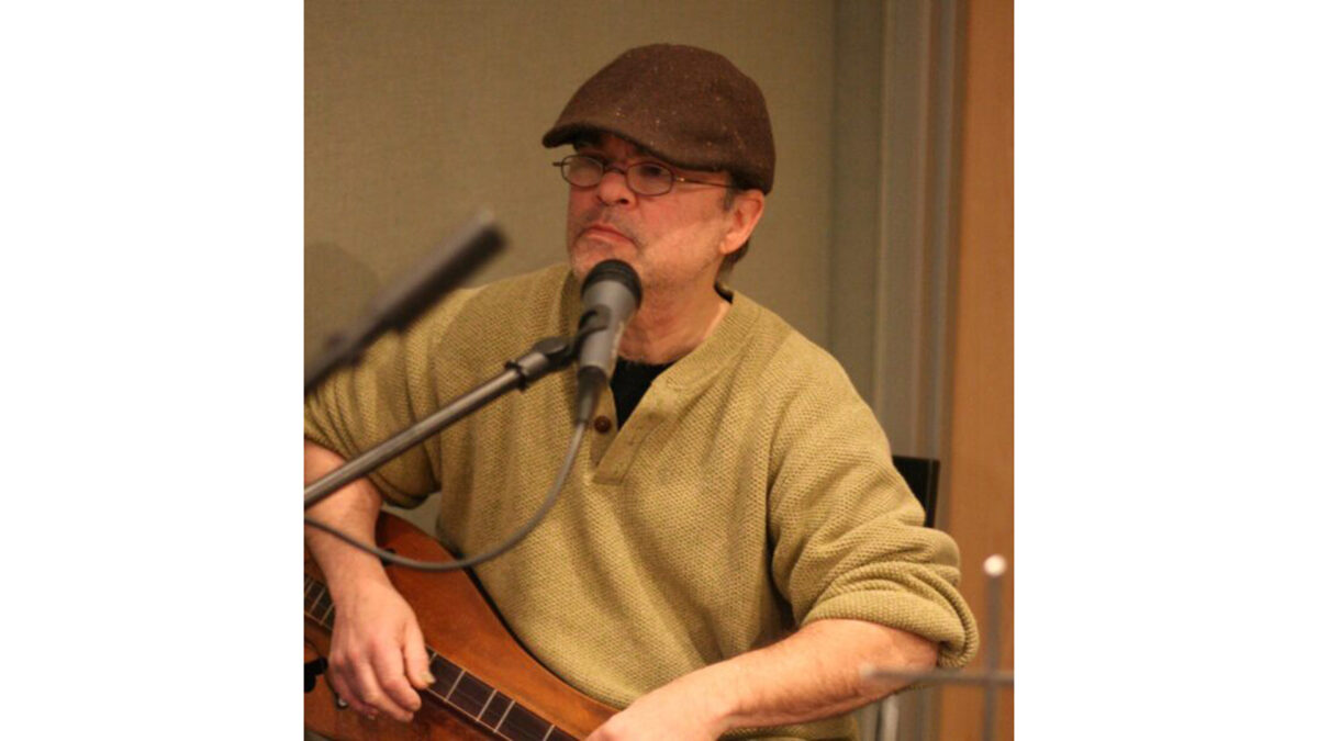 Jeff-Berman_wp An adult holding a dulcimer and sitting behind a microphone in a radio studio