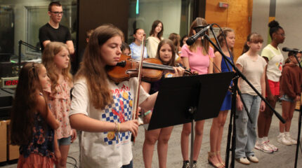 Fourteen youth singing in a choir and a teen playing a violin
