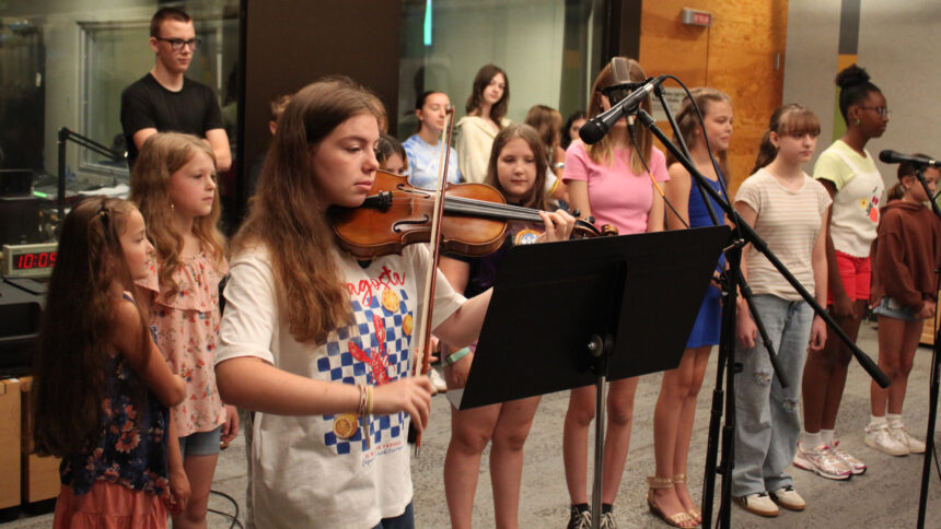 Fourteen youth singing in a choir and a teen playing a violin