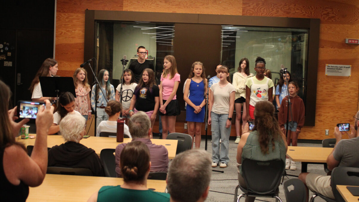 Fourteen youth singing in a choir and a teen playing a violin