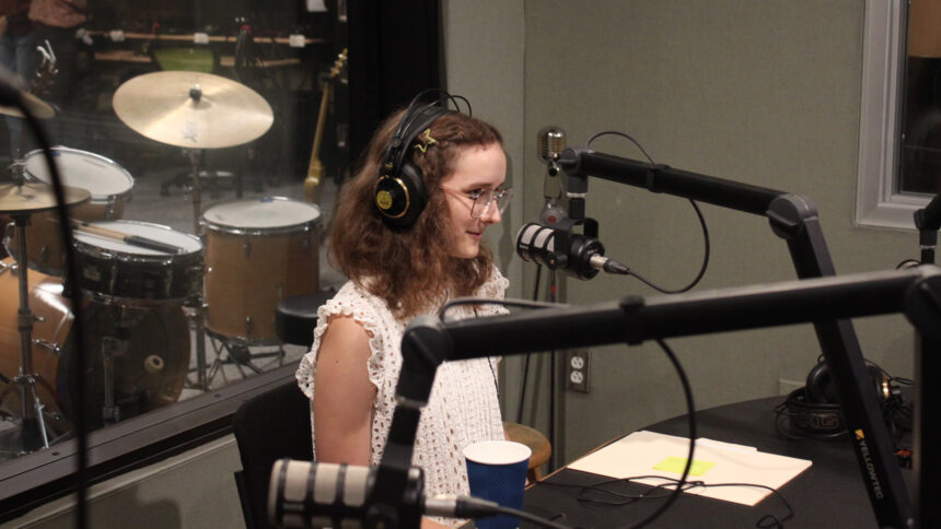 A teen wearing headphones speaking into a microphone in a radio studio