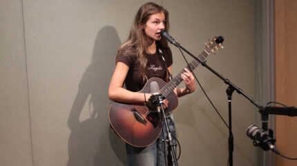 A teen playing acoustic guitar and singing into a microphone in a radio studio