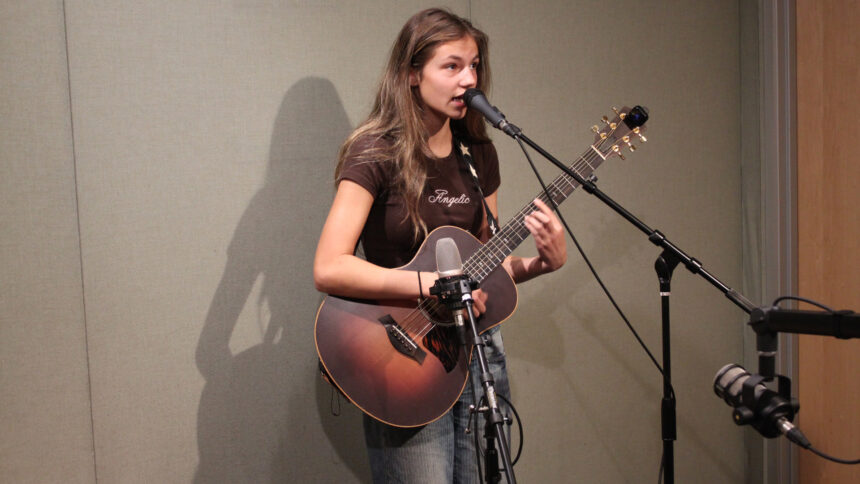 A teen playing acoustic guitar and singing into a microphone in a radio studio