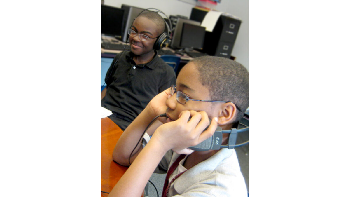 Two youth wearing headphones sitting at a brown table