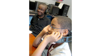 Two youth wearing headphones sitting at a brown table