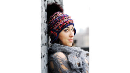 An adult wearing a knit hat leaning against a gray wall.