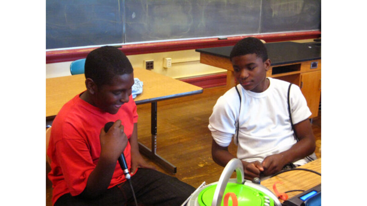 Two youth looking at a cd player, one of the youths holding a microphone