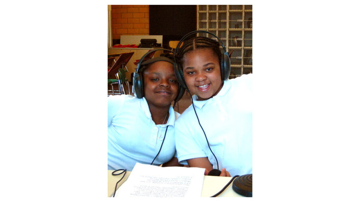 Two youth wearing headphones smiling at the camera