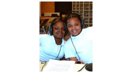 Two youth wearing headphones smiling at the camera