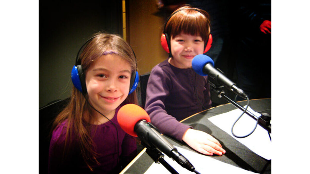 girls_wp Two youth wearing headphones smiling and sitting behind microphones in a radio studio