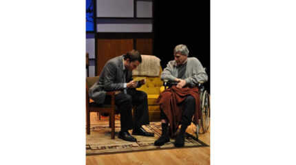 An adult sitting in a chair and an adult in a wheelchair looking at the same piece of paper