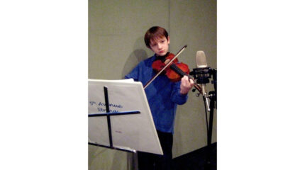 A youth playing a violin and looking at sheet music on a music stand in a radio studio