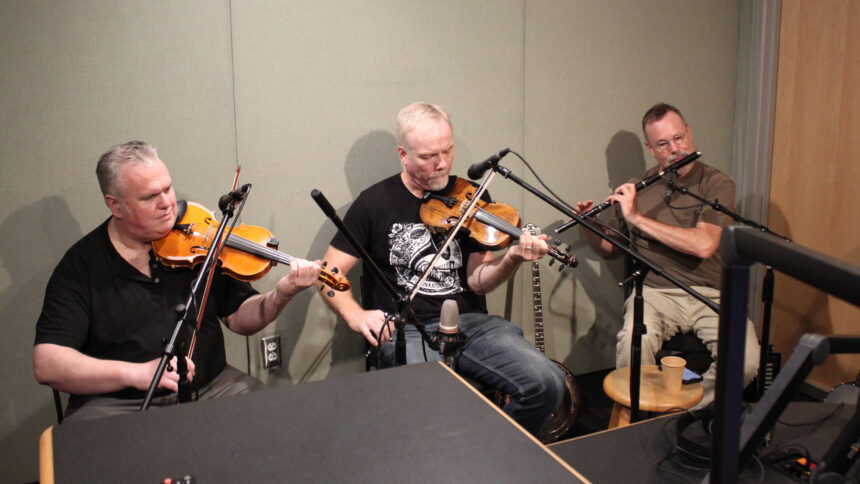 Two adults playing violins and an adult playing a tin whistle in a radio studio