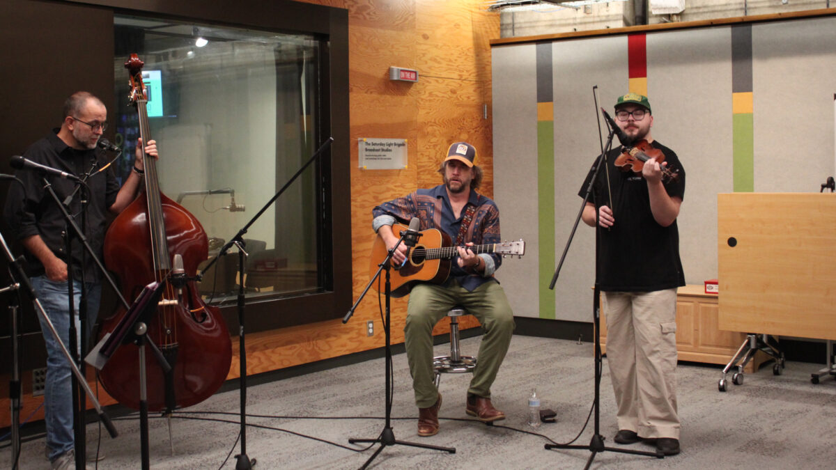 City-Holler-Band-1 An adult holding an upright bass, an adult playing an acoustic guitar, and an adult playing a fiddle
