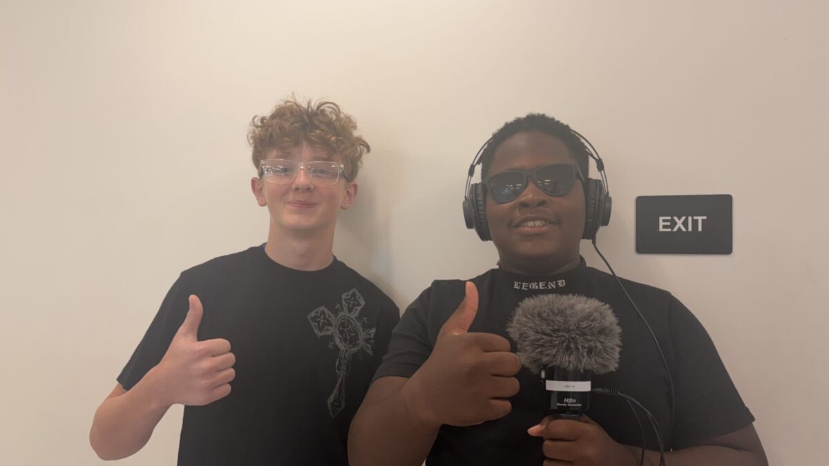 IMG_1837 Two youth flashing a thumbs up, one wearing headphones and sunglasses and holding a microphone.