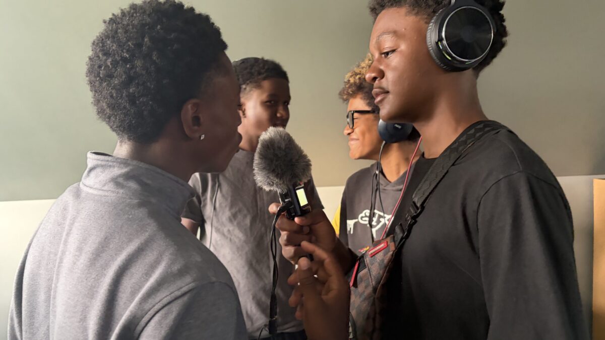 IMG_1840 Two youth wearing headphones and holding microphones interviewing two other youth