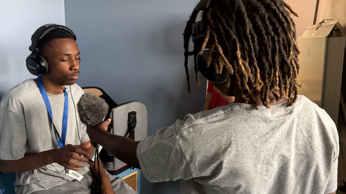 IMG_1850 A youth wearing headphones and holding a microphone interviewing another youth wearing headphones