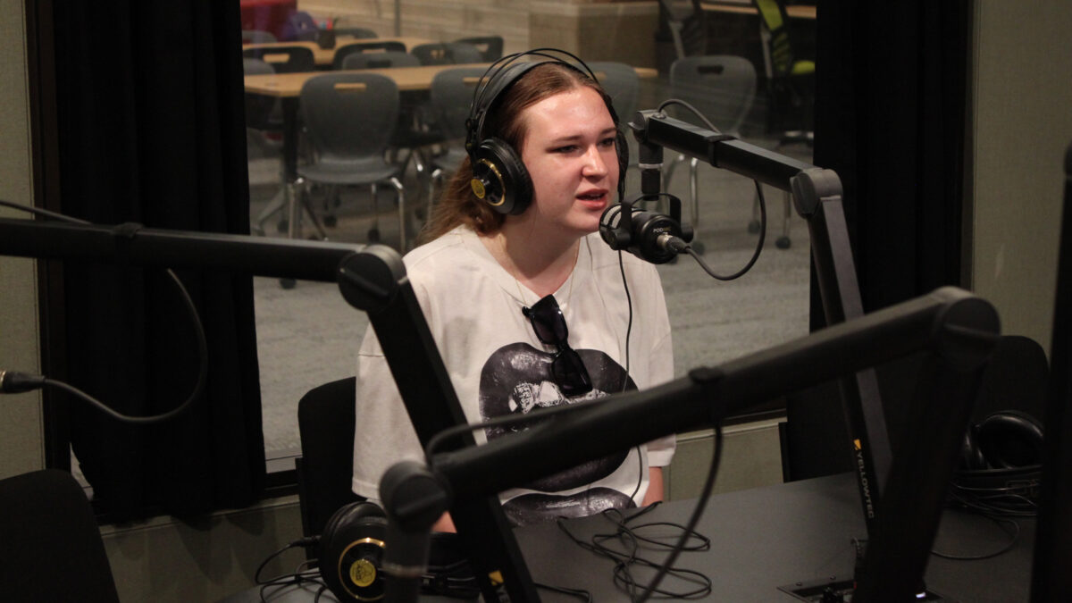 A teen wearing headphones speaking into a microphone in a radio studio