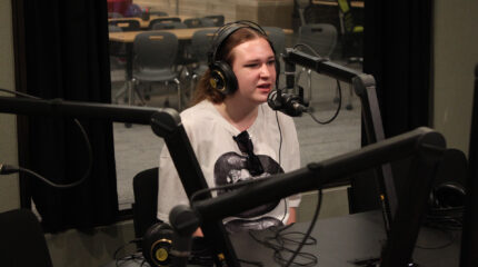 A teen wearing headphones speaking into a microphone in a radio studio