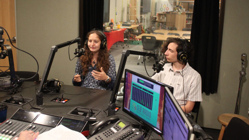 Two teens wearing headphones speaking into microphones being interviewed in a radio studio