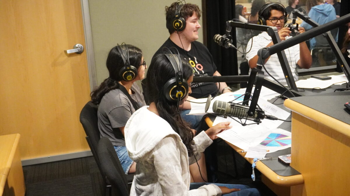 Streaming-Labor-2026_3 Four teens wearing headphones speaking into microphones in a radio studio