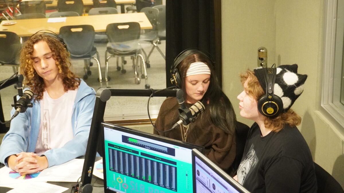 Streaming-Labor-2026_6 Three teens wearing headphones sitting behind microphones in a radio studio