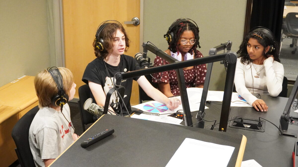 Streaming-Labor-2026_7 Four teens wearing headphones speaking into microphones in a radio studio