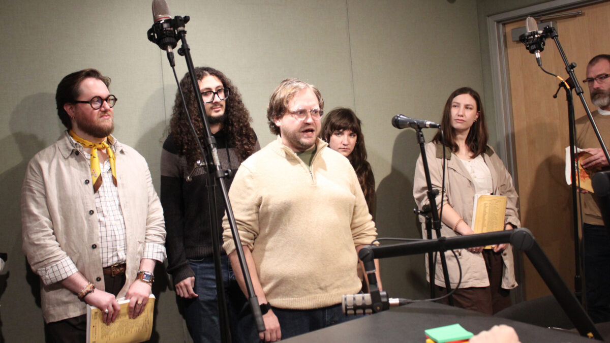Pittsburgh-Savoyards-2 Six adults standing behind microphones, one singing, in a radio studio