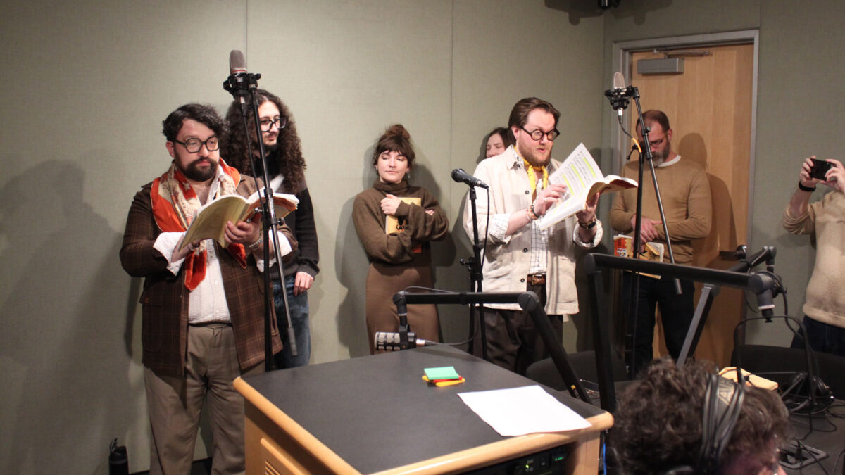 Pittsburgh-Savoyards-5 Six adults standing behind microphones, two singing, in a radio studio