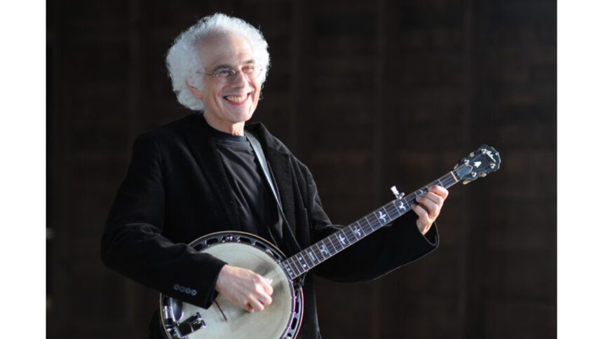 An adult smiling while playing a banjo